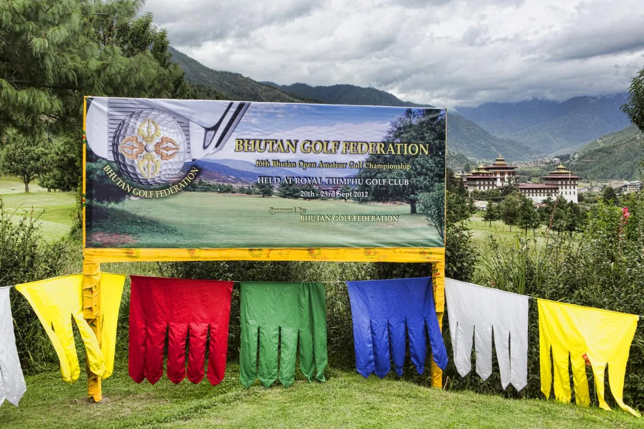 The entrance area at Royal Thimphu Golf Club, with a Bhutan Golf Federation banner and the mountain setting beyond.